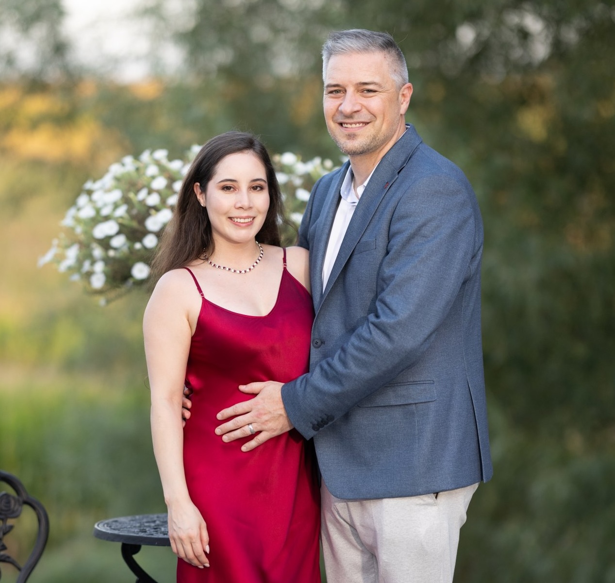 Brent and Leidy standing together outdoors, Leidy in a red dress and Brent in a grey jacket